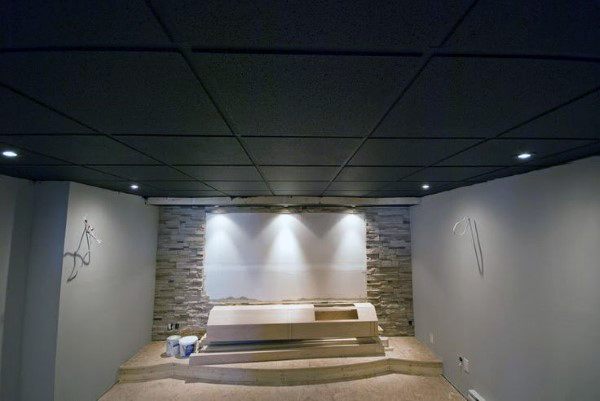 Basement with black drop ceiling, recessed lighting, and stone accent wall under construction.