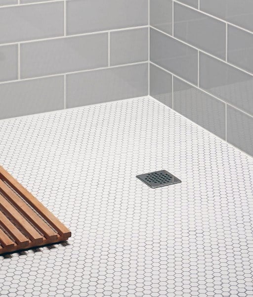 Shower with white hexagonal honeycomb floor tiles, gray subway walls, and wooden bath mat.
