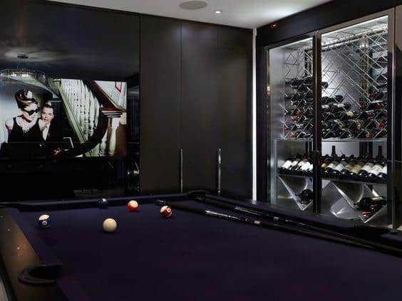 Modern billiard room with black felt table, wine storage, and a stylish entertainment setup.