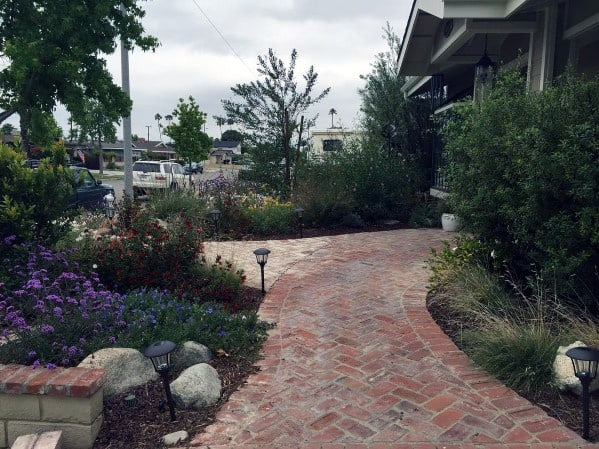Charming curved brick walkway surrounded by colorful flowers, greenery, and garden lights, leading to a welcoming home entrance
