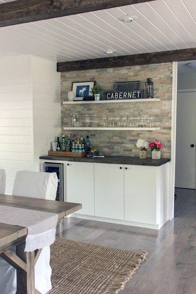 Basement bar area with rustic shiplap ceiling, stone backsplash, and wooden dining table.