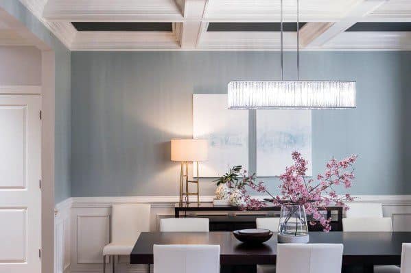 Dining room with light blue walls, chair rail, table with pink flowers, and modern chandelier