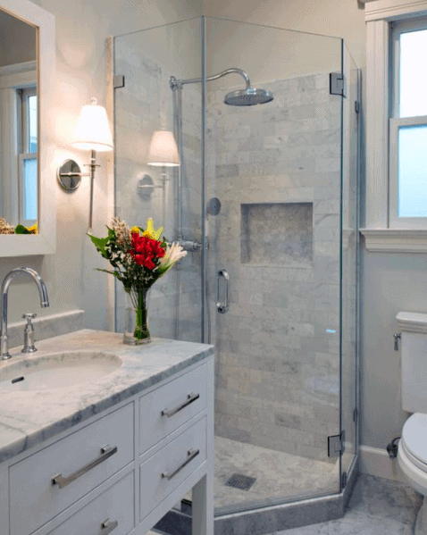 An elegant bathroom with a corner glass shower, marble vanity, and fresh flowers on the counter