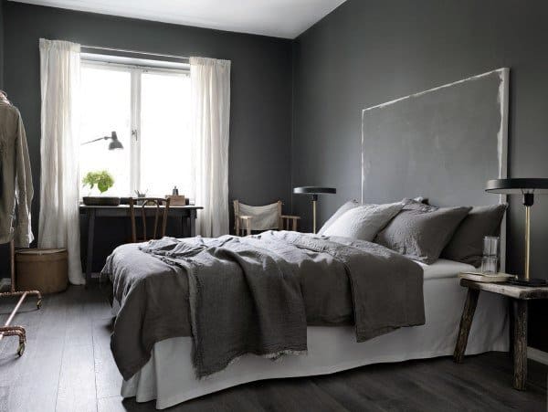 Minimalist bedroom with grey walls, a bed with grey bedding, and a desk by the window featuring a plant and lamp