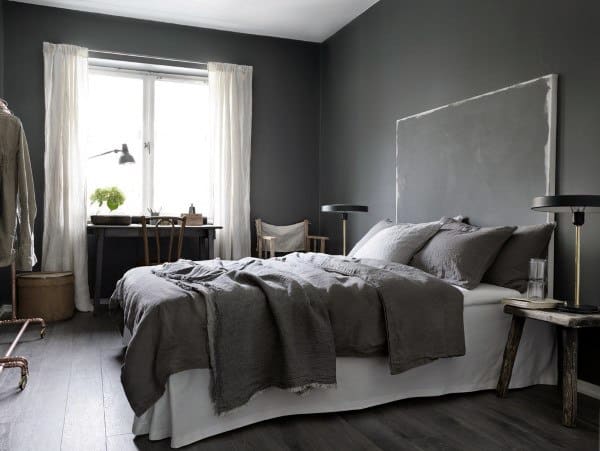 Minimalist bedroom with dark grey walls, a bed with gray linens, wooden nightstands, and a window with sheer curtains