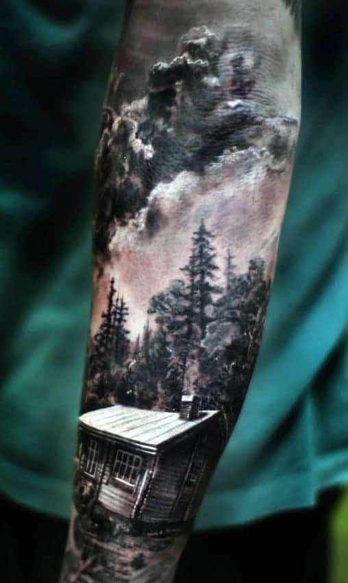 A forearm tattoo of a cabin in the woods with a cloudy sky background