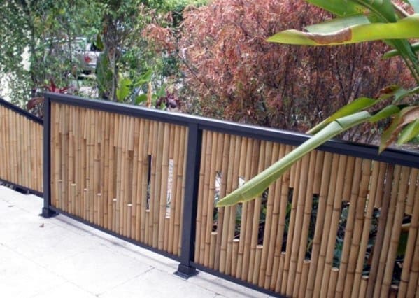 Metal-framed bamboo fence with unique staggered bamboo design along a garden pathway surrounded by vibrant plants.