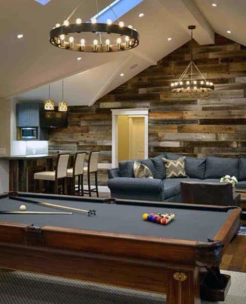 Rustic game room with pool table, reclaimed wood accent wall, sectional sofa, and home bar.