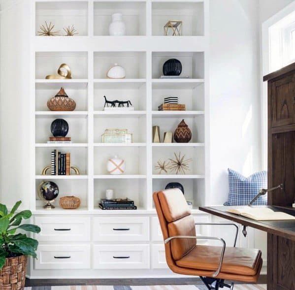 Bright home office with white built-in bookcase, decorative accents, leather chair, and natural light through large windows