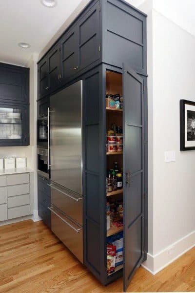 Tall pantry cabinet with navy blue doors beside a stainless steel refrigerator.