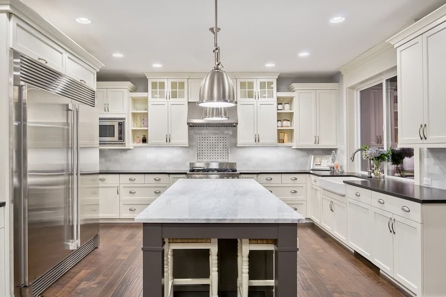 Modern kitchen with white cabinets, large fridge, island seating with stools, and pendant lighting