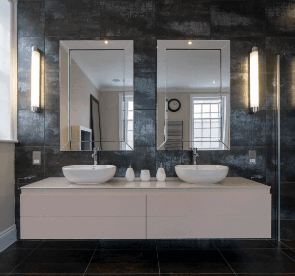 Modern bathroom with double sinks, rectangular metallic-framed mirrors, and dark textured walls.