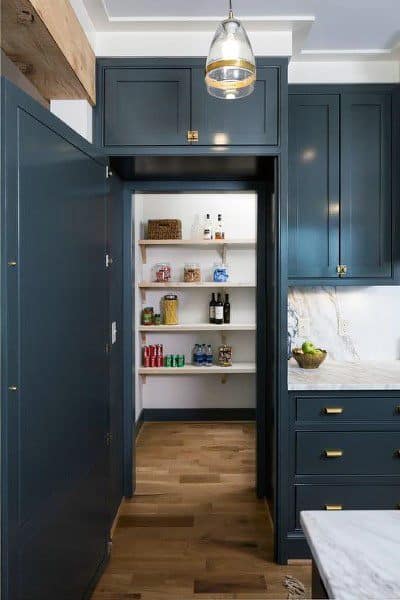 Walk-in pantry with white shelves and navy cabinets in a modern kitchen.