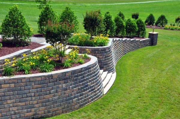 Curved brick retaining walls with tiered flower beds, shrubs, and integrated stone steps.