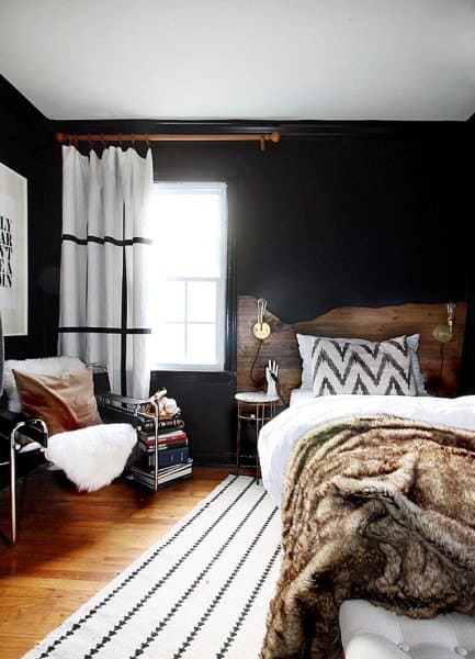 ustic bedroom with wooden headboard, black accent wall, fur blanket, and striped rug.