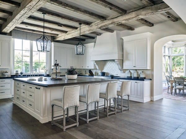 Rustic kitchen with white cabinets, wooden beams, large island, and pendant lighting.