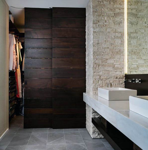 A modern sliding closet door made from dark wood panels, offering a sleek and sophisticated look that complements the stone wall and minimalist design