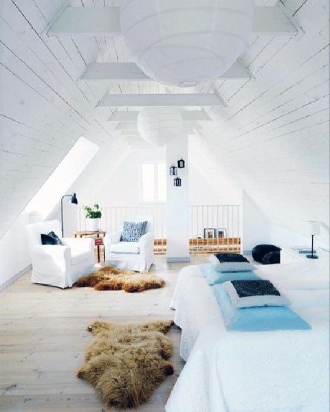 Cozy attic room with white decor, a comfy bed, armchairs, and a fur rug on wooden flooring