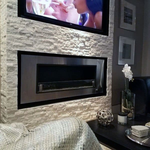 Modern stacked stone fireplace with a sleek stainless steel insert and mounted TV in a cozy living space