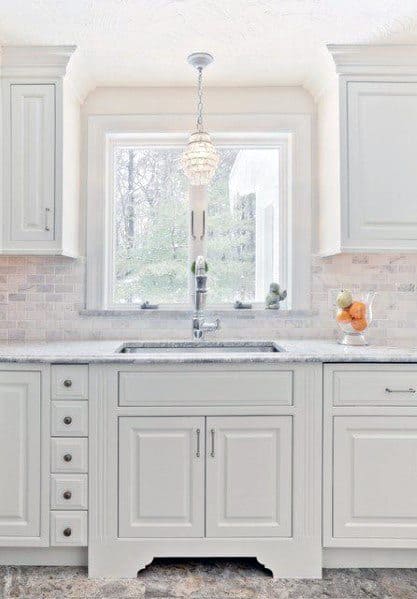 Bright kitchen with white cabinetry, a light stone backsplash, a farmhouse sink, and a pendant light over the window