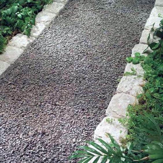 A gravel walkway bordered with traditional stone edging, surrounded by greenery, creating a natural and inviting path