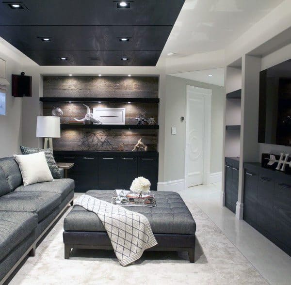 Modern basement with black panel ceiling, recessed lighting, sectional sofa, and decorative shelving.