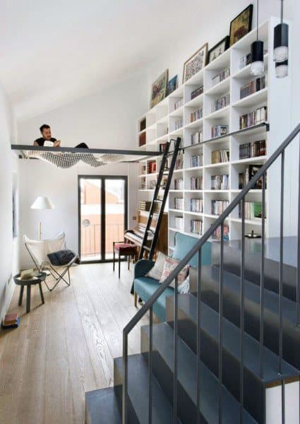 Net hammock above a stylish reading nook with floor-to-ceiling bookshelves and modern decor.