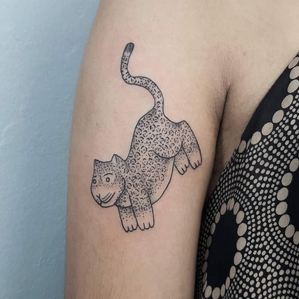 A playful and minimalist tattoo of a jaguar, featuring dotwork shading and a cartoonish design, placed on the upper arm.