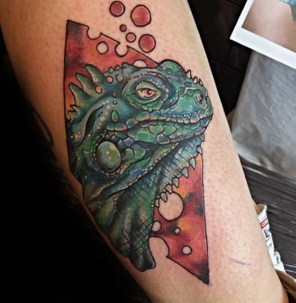 Artistic iguana tattoo with a green-blue color palette, set inside a pink geometric frame with bubble-like cutouts.