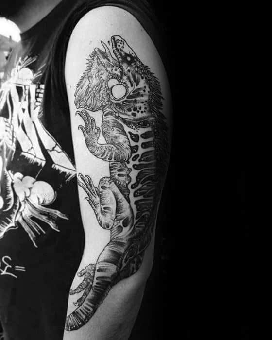 Detailed blackwork iguana tattoo on upper arm with bold shading, fine line textures, and a dynamic climbing pose.