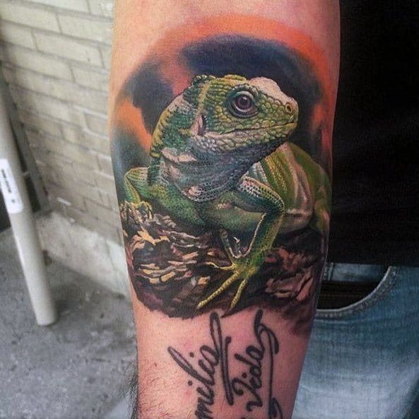 Vivid green iguana tattoo perched on a rock with a dramatic orange and black sky background, detailed with lifelike texture and shading.