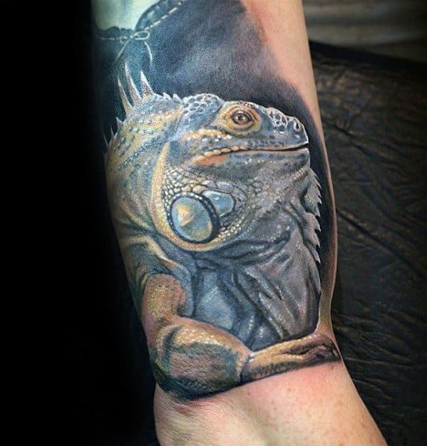 Hyper-realistic iguana tattoo with soft beige and grey tones, detailed texture, and a calm expression resting on the forearm.