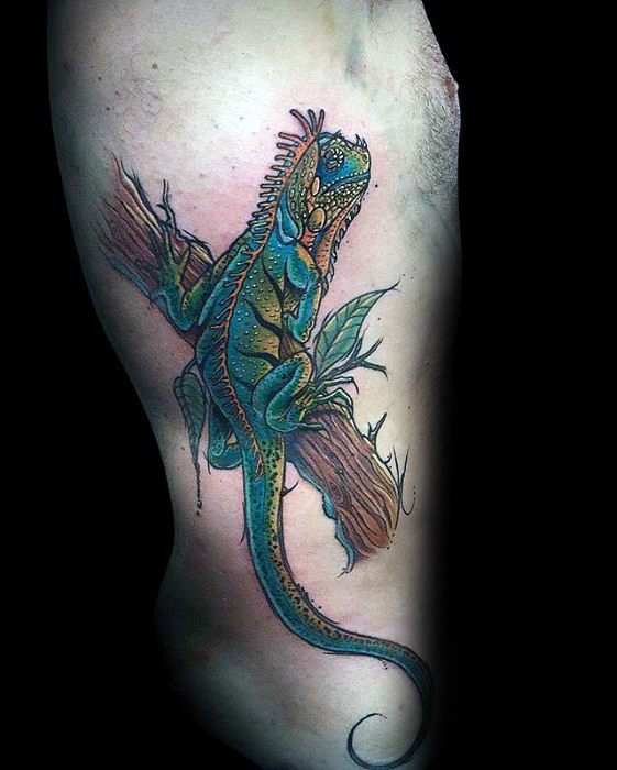 Colorful iguana tattoo crawling on a branch with bold blue, green, and orange hues, long tail, and stylized leaves for added detail.