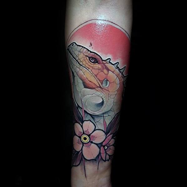 Stylized iguana tattoo with soft orange tones, set against a red sun and floral accents for a modern, artistic look on the forearm.