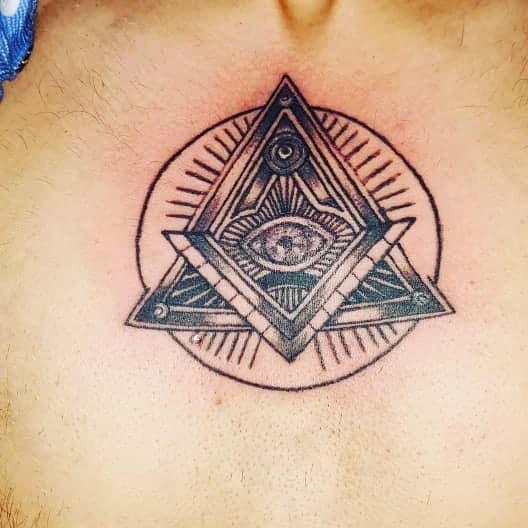 Tattoo of an all-seeing eye inside an intricate geometric pyramid with radiating lines, inked in black on the chest.
