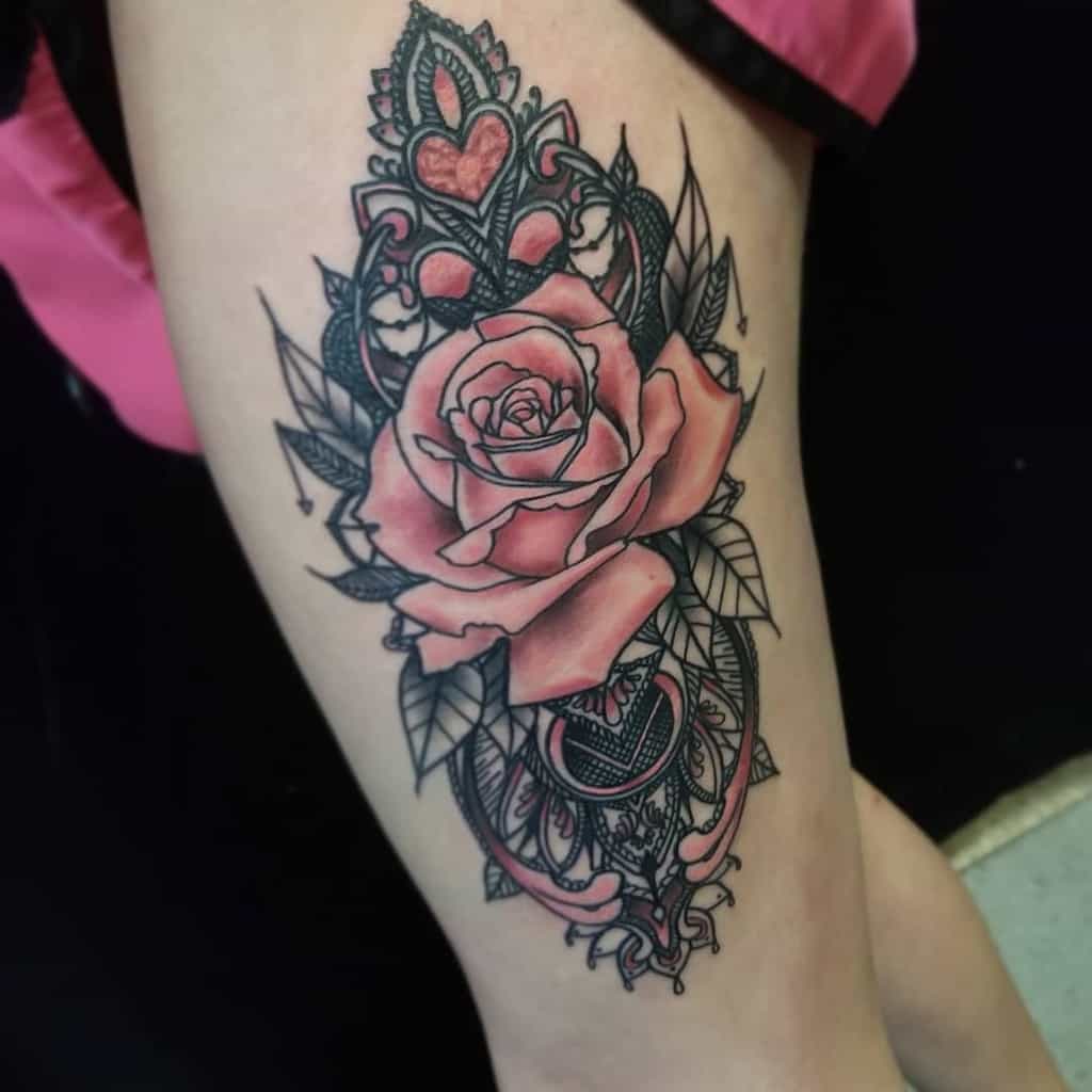 Ornate tattoo featuring a vibrant pink rose with intricate lace filigree, heart accents, and delicate ornamental details.