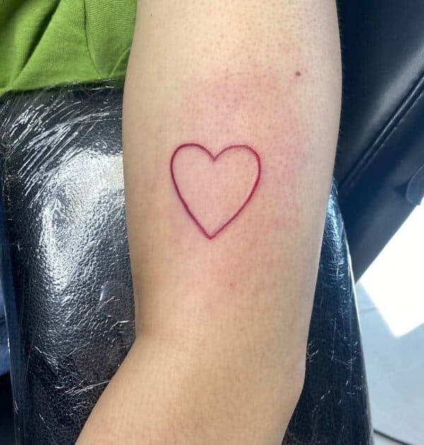 Simple heart outline tattoo in red ink on an inner arm