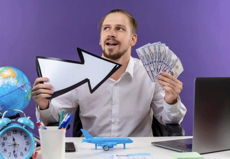 Smiling man at a desk holds a fan of cash, with an arrow and Cyprus salaries 2025 data on a purple background