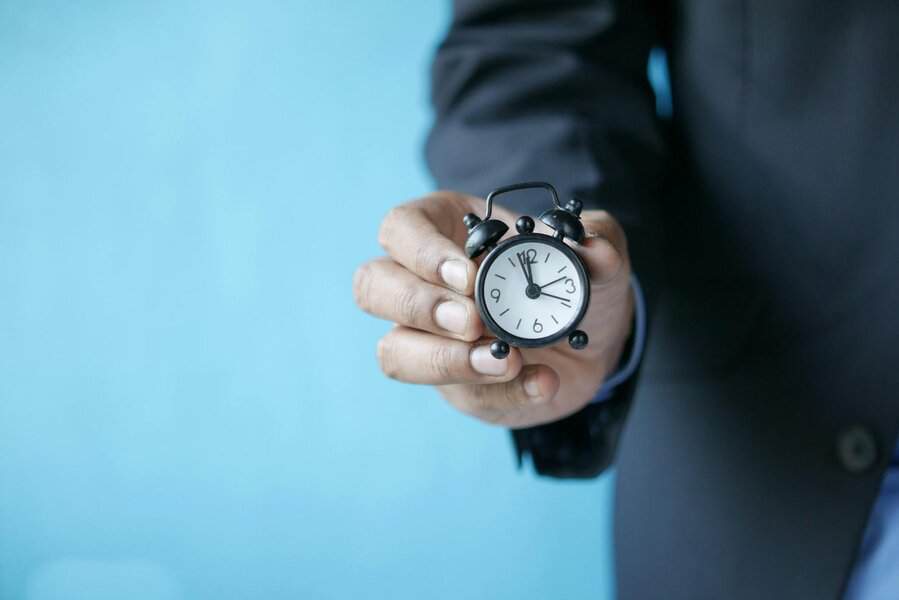 A modern professional in a suit holds a small black alarm clock with a light blue background