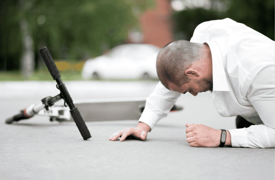 A man in a white shirt lies on the ground after falling off his scooter—fall detection could help alert someone nearby