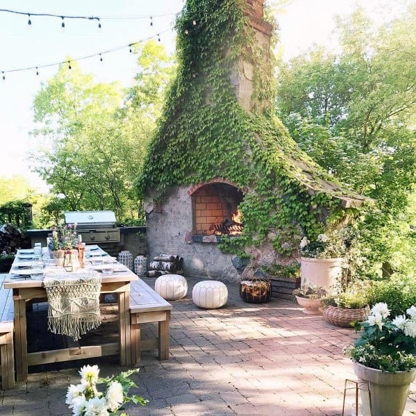 Brick patio with ivy-covered fireplace, wooden table, and decorative string lights