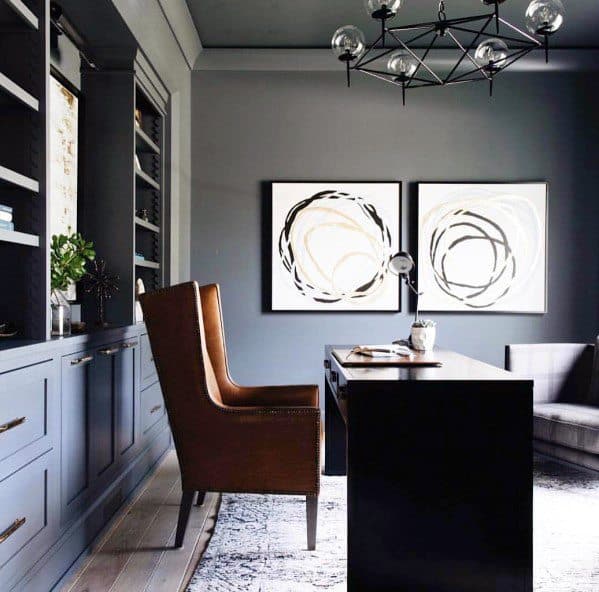 Modern office with gray built-in bookcases, sleek black desk, leather armchair, abstract art, and geometric chandelier