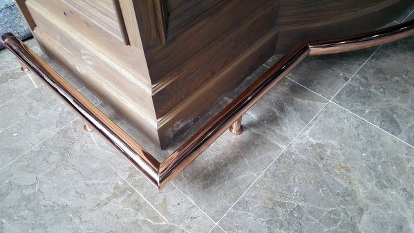 Copper-plated foot rail with rounded corners, installed around a wooden bar on polished marble flooring.