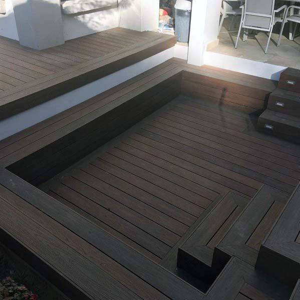 Wooden step seating around a recessed patio area with bench-like tiers, sunlight casting charming shadows