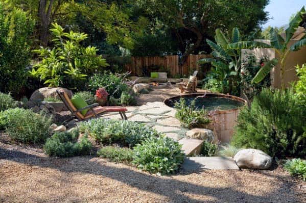 Lush garden with a stone path, lounge chair, and small pond surrounded by plants and trees