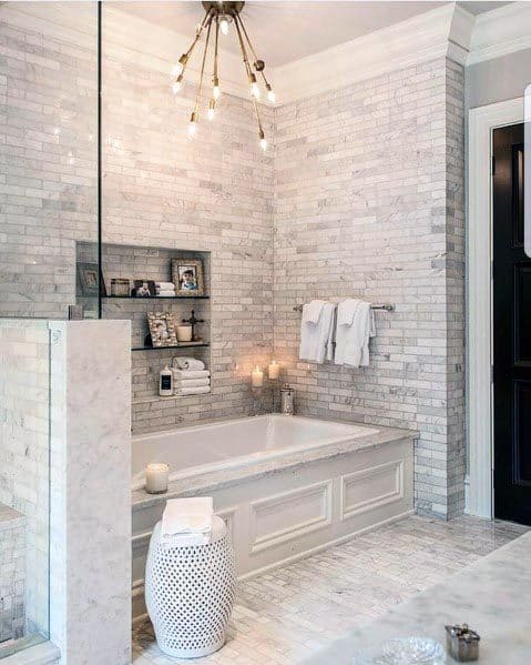 Elegant bathroom design featuring grey marble tiles, built-in shelving for essentials, and a luxurious soaking tub with detailed paneling.