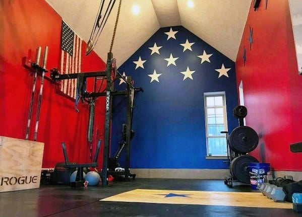 Patriotic-themed home gym with red, white, and blue walls, weightlifting platform, and Rogue equipment.