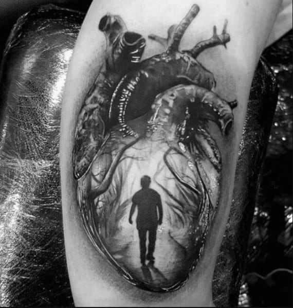 Black and white tattoo of an anatomical heart with a silhouette of a person walking inside it on an arm