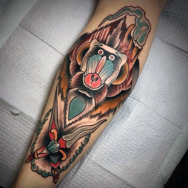 Neo-traditional baboon tattoo with bold outlines, earthy tones, and a dynamic pose, featuring a dagger and beaded elements for a striking design.