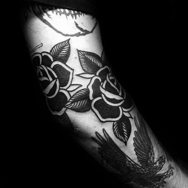 Black and white tattoo of roses and a bird on a person's forearm